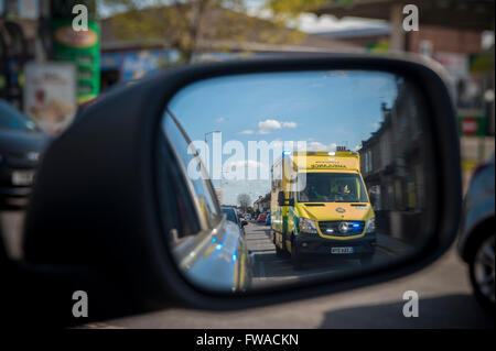 Ein Rennsport-Krankenwagen mit Blaulicht überholt ein Auto, das es in seiner Flügel Spiegel sieht Stockfoto