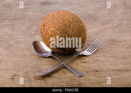 Kokosnuss auf einem hölzernen Hintergrund, Gabel mit Löffel ist Crosswised davor Stockfoto