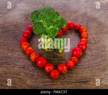 Brokkoli wie ein Baum auf eine hölzerne Struktur auf einem weißen Hintergrund, umgeben von roten Kirschtomaten Stockfoto