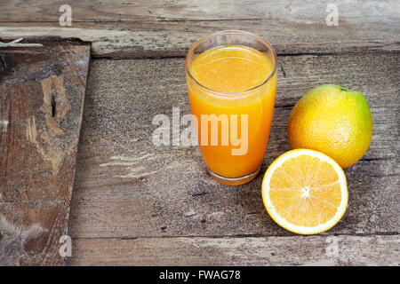 Orange in zwei Hälften geschnitten und in dünne Scheiben geschnitten und frisch gepressten Orangensaft im Glas auf alten Tisch Holz Stockfoto
