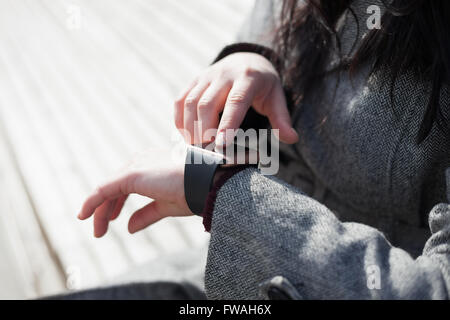 Weibchen mit ihren trendigen intelligente Armbanduhr auf der Bank sitzen. Diese Person ist immer mit social Media und Internet verbunden. Stockfoto