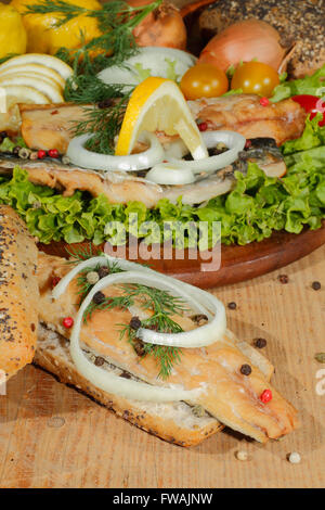 Geräucherte Makrelen-Filet, garniert mit Zwiebelringen, in Vollkornbrot mit Salat auf ein Schneidbrett aus Holz Stockfoto