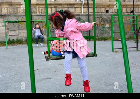 Junges Mädchen mit Spielzeug auf Schaukel Rückblick auf die große Schwester. Kinder spielen auf der Schaukel auf einem Spielplatz in Baku, Aserbaidschan Stockfoto