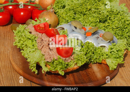 Zwei Fische Brötchen mit Thunfisch und sauren Hering, garniert mit Salat, Tomaten, Zwiebeln und Gurken auf einem Holzbrett Stockfoto