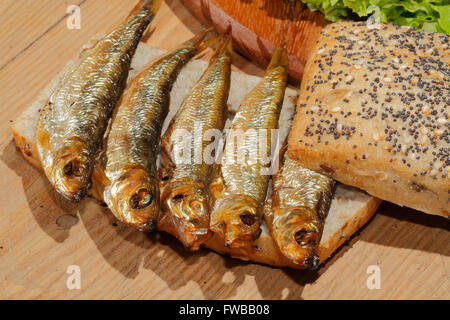 Geräucherte Sprotten in Vollkornbrot mit Salat auf ein Schneidbrett aus Holz Stockfoto