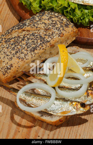 Geräucherte Sprotten mit Salat, Zitrone, Zwiebeln Tomaten, garniert mit Dill auf einem Brett aus Holz Küche Stockfoto