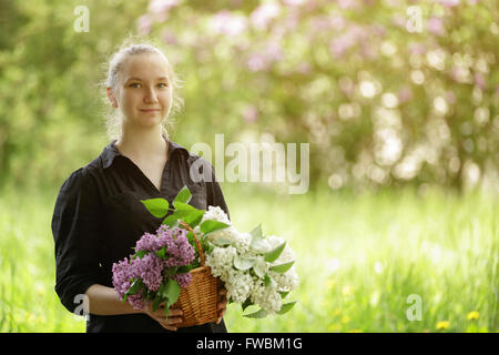 Weibliche Teenager-Mädchen halten Korb voller lila Blumen Stockfoto