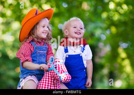 Kleine Jungen und Mädchen verkleidet als Cowboy und Cowgirl mit Spielzeug Schaukelpferd im Park zu spielen. Kinder spielen im Freien. Stockfoto