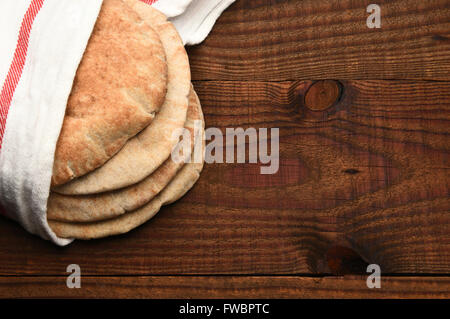 Vollkorn Fladenbrot auf einem rustikalen Holztisch mit Textfreiraum. Das Brot ist in ein Handtuch gewickelt und von einem hohen Winkel gesehen. Stockfoto