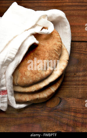 Vollkorn Fladenbrot auf einem rustikalen Holztisch mit Textfreiraum. Das Brot ist in ein Handtuch gewickelt und von einem hohen Winkel gesehen. Verti Stockfoto