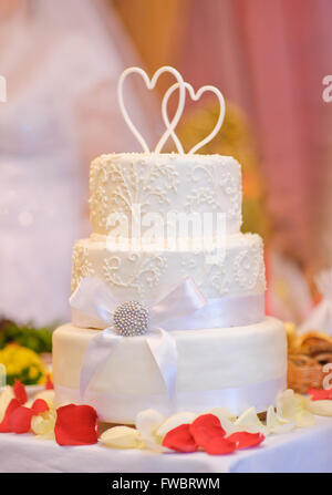 Multi-tiered weiße Hochzeitstorte mit oben zwei Herzen Stockfoto