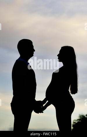 Ein junger Mann und seine schwangere Frau bei Sonnenuntergang. Silhouetten Stockfoto