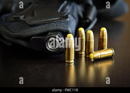 Pistole in einem Holster und mehrere Kugeln auf einem dunklen Tisch Stockfoto