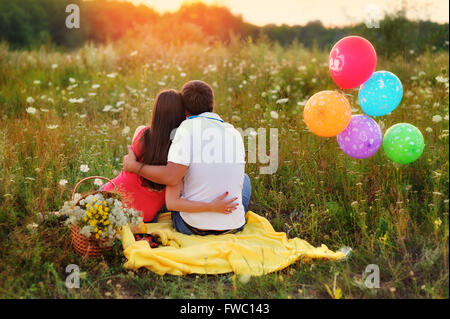 Mann und Frau sitzen auf dem Gebiet und bunten Luftballons Stockfoto