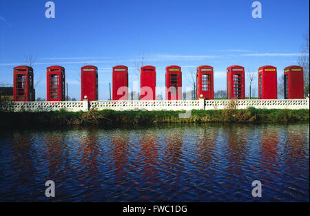 Sammlung von roten Telefonzellen aufgereiht und am Rande eines kleinen Sees, die die Farbe und Form im Wasser. Stockfoto