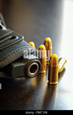 Pistole in einem Holster und mehrere Kugeln auf einem dunklen Tisch Stockfoto