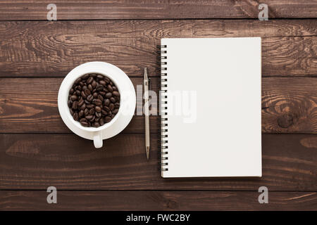 Kaffeebohnen in Tasse und Buch leere Seite auf Holztisch Stockfoto