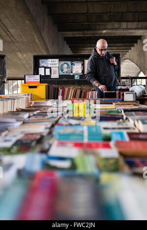 Ein Mann Suche gebrauchte Bücher bei einem Outdoor-Buchmarkt unter Waterloo Bridge in London. Stockfoto
