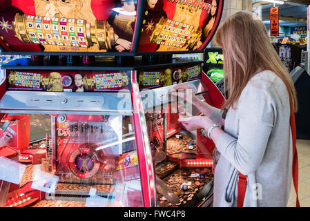 Eine Frau spielt eine 2P billiges Nudger Maschine in einer Kirmes in einem britischen Badeort. Stockfoto