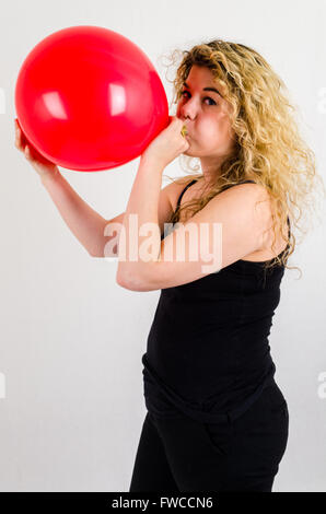 Einzelne Erwachsenfrau Sprengung ein Medium sized roten Ballon Stockfoto