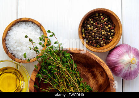 Top-flachen Ansicht der Zutaten: Salz, Pfeffer, Chili, Thymian, Knoblauch, Olivenöl in Schalen auf weißem rustikalen Holztisch Stockfoto