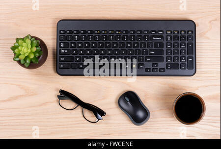 Draufsicht auf einen sauberen Schreibtisch bestehend aus Kaffee, Babypflanze, Computer-Tastatur und Maus, und eine Lesebrille. Stockfoto