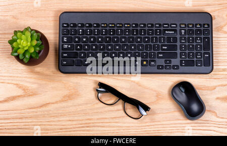 Draufsicht auf einen sauberen Schreibtisch bestehend aus Computer-Tastatur, Maus, Babypflanze und Lesebrille. Stockfoto