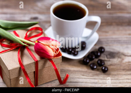 Einzelne Tulpe ruht auf Geschenk-Box mit einer Tasse Kaffee und dunkler Schokolade im Hintergrund auf rustikalen Holz. Selektiven Fokus auf Vorderseite Stockfoto