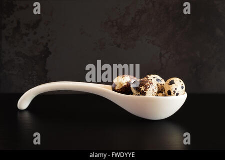 Wachteleier in einem keramischen Löffel auf einem schwarzen Holztisch. Stockfoto
