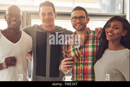 Gruppe von vier schwarzen, weißen und Hispanic glücklich nach Freunde legere Kleidung und halten Getränke während jeder umarmt Stockfoto