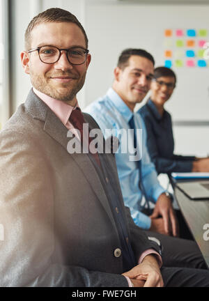 Gut aussehender bärtiger Mann mit Anzug und Krawatte mit zwei Kollegen des Managements in der Sitzung am Tisch vor der großen weißen Stockfoto