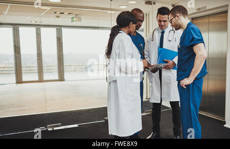 Diverse multirassischen medizinisches Team Beratung auf einer Patientenakte in einem Foyer stehen in einem Krankenhaus um einen Tablet compu gruppiert Stockfoto