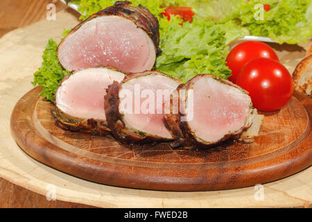 Schweinefilet, Medaillons, eingewickelt in Speck, Fleisch vom Grill und garniert mit Salat und Tomaten auf einem Holzbrett Stockfoto