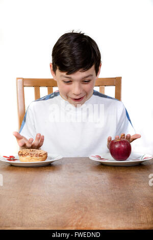 Ein junger Teenager Blick auf einen Donut und ein Apfel entscheiden, was man zu essen. Stockfoto