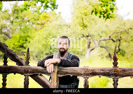 Bärtiger jungen Mann stützte sich auf einen alten geschnitzten hölzernen Zaun. Stockfoto