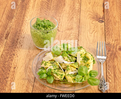 Glas-Teller mit Basilikum-Ricotta-Tortelloni mit Pesto und Parmesan Flocken und Silber Gabel. Stockfoto