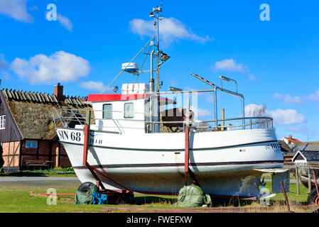 Kivik, Schweden - 1. April 2016: Weiße Fischerboot auf Anhänger in einem Fischerdorf. Haus und bewölktem Himmel im Hintergrund. Stockfoto