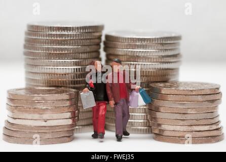 Ein Miniatur-paar tragen shopping Taschen stehen zwischen Stapeln von Münzen. Stockfoto