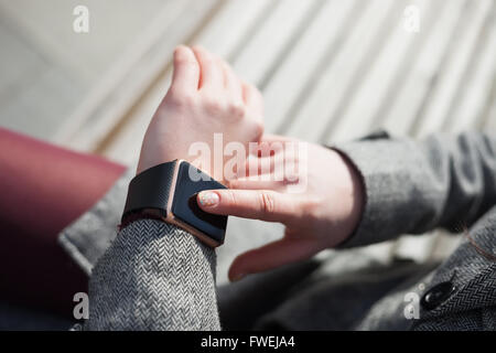 Weibchen mit ihren trendigen intelligente Armbanduhr auf der Bank sitzen. Diese Person ist immer mit social Media und Internet verbunden. Stockfoto