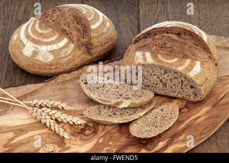 Frische hausgemachte Rye Brotkruste auf einem Oliven Holz Brett mit Weizen scheiden über Eiche Hintergrund. Stockfoto