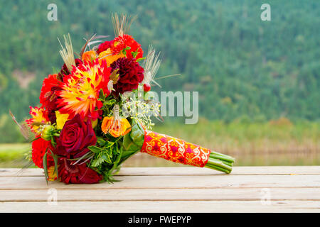 Ein Brautstrauß Hochzeit sitzt auf einem hölzernen Dock mit einer malerischen Kulisse von Bergen und Bäumen. Stockfoto