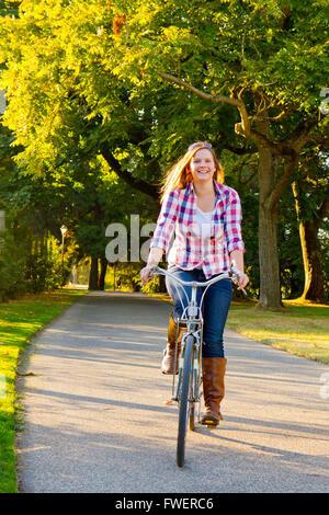 Eine attraktive Frau fährt Fahrrad auf einem Weg durch einen Park. Stockfoto