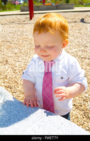Ein kaukasischer Baby junge spielt im Park tragen ein weißes Hemd und eine Krawatte. Stockfoto