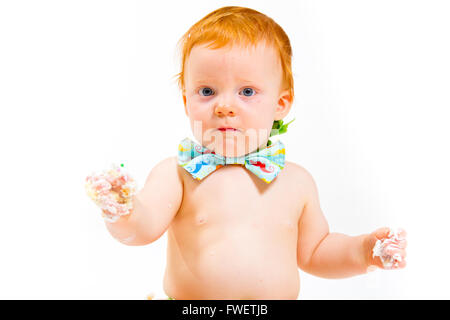 Ein Baby bekommt, Kuchen zum ersten Mal an seinem ersten Geburtstag in diesem Kuchen smash im Studio vor einem weißen Hintergrund zu essen. Stockfoto