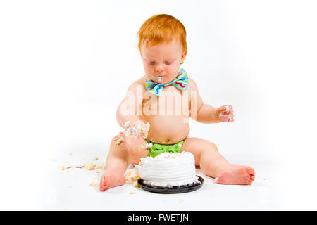 Ein Baby bekommt, Kuchen zum ersten Mal an seinem ersten Geburtstag in diesem Kuchen smash im Studio vor einem weißen Hintergrund zu essen. Stockfoto