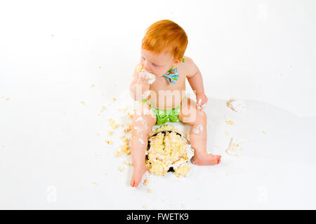 Ein Baby bekommt, Kuchen zum ersten Mal an seinem ersten Geburtstag in diesem Kuchen smash im Studio vor einem weißen Hintergrund zu essen. Stockfoto