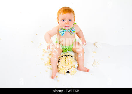 Ein Baby bekommt, Kuchen zum ersten Mal an seinem ersten Geburtstag in diesem Kuchen smash im Studio vor einem weißen Hintergrund zu essen. Stockfoto