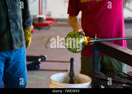 Zwei Männer arbeiten hart daran, um ein einzigartiges Kunstwerk aus geschmolzenem Glas zu schaffen. Sie sind Glasbläserei in einem Studio in Oregon. Stockfoto