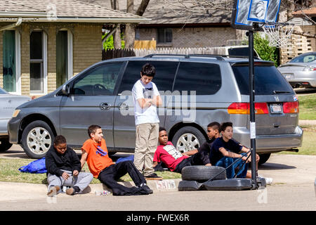 Sechs preteen Knaben machen Sie eine Pause vom spielen Basketball und sitzen auf einem Bordstein Nachbarschaft zusammen in Oklahoma City, Oklahoma, USA. A Stockfoto