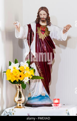 Statue von Jesus Christus mit dem Heiligen Herzen und Frühling Narzissen im Inneren einer Kirche. Stockfoto